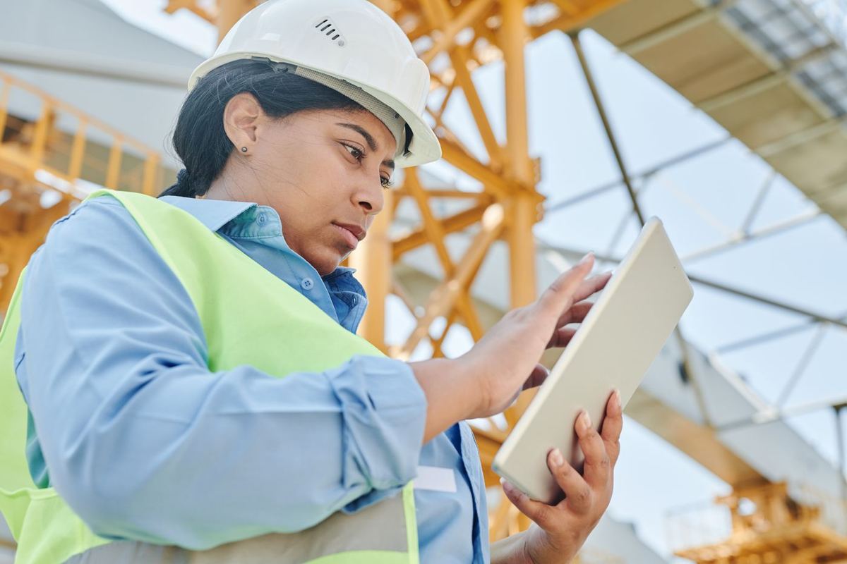 Site engineer in a helmet and safety vest using a tablet in front of a steel frame